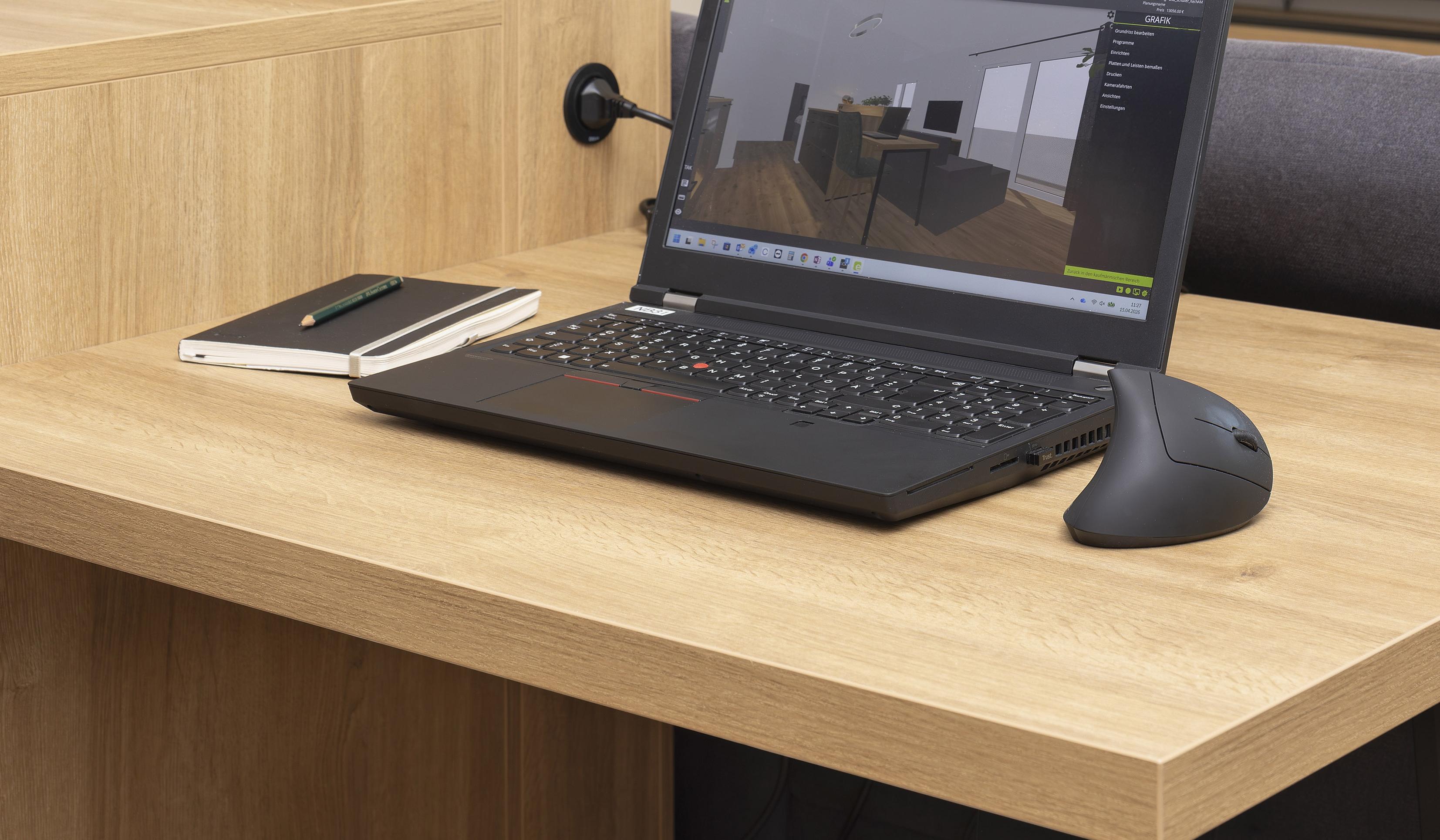 Laptop, Maus und Notizbuch auf Holztisch mit schwarzem Hocker und Pflanzen im Hintergrund.
