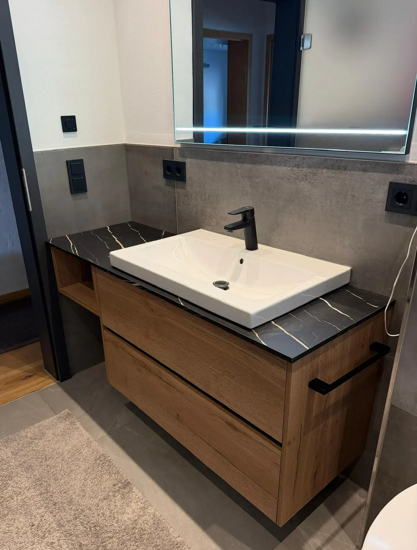 Modernes Waschbecken mit Holzunterschrank, schwarzer Armatur und großem Spiegel.