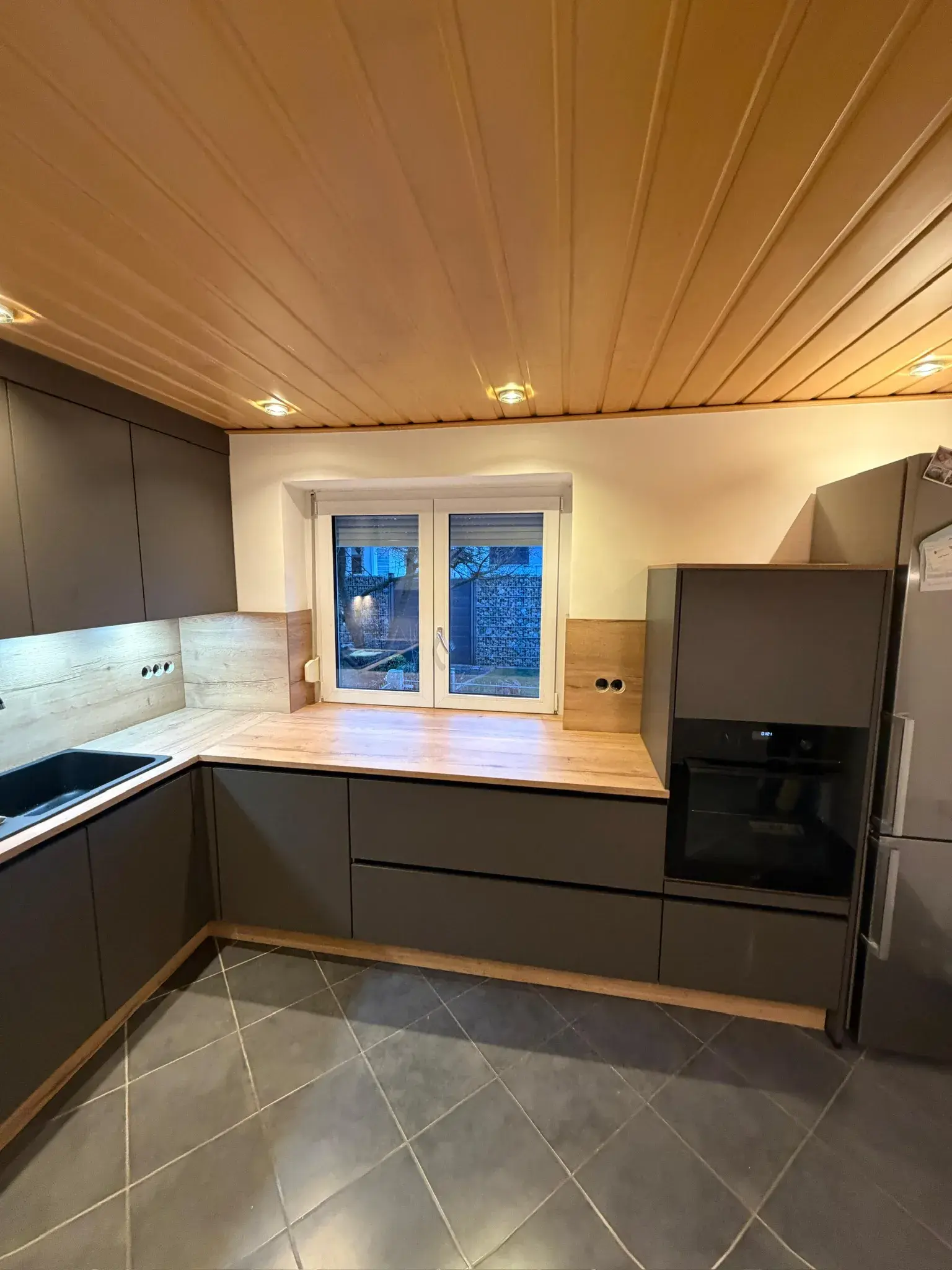 Moderne Küche mit dunklen Schränken, Holzarbeitsplatte und Fenster, Fliesenboden