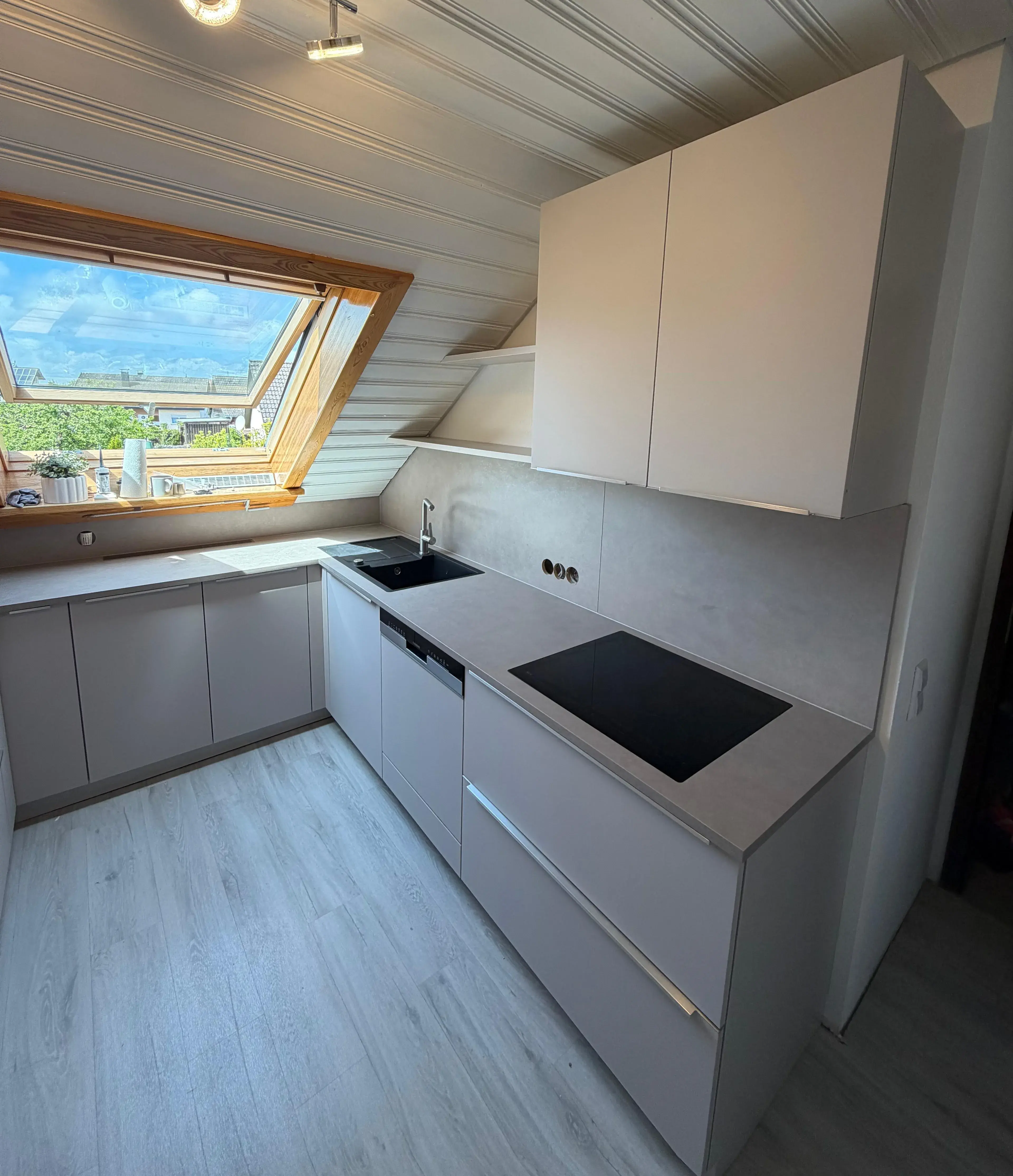 Moderne Dachgeschossküche mit hellen Schränken und großem Fenster, viel Tageslicht.