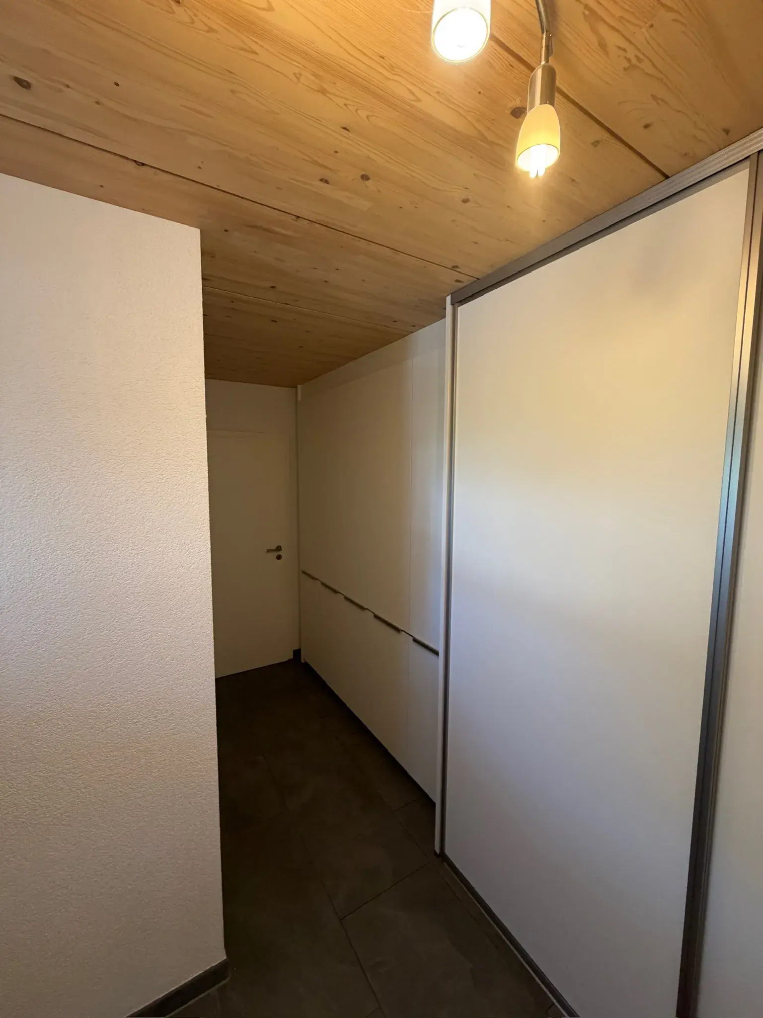 Schmaler Flur mit Holzdecke, weißen Wänden und geschlossenen Schränken.