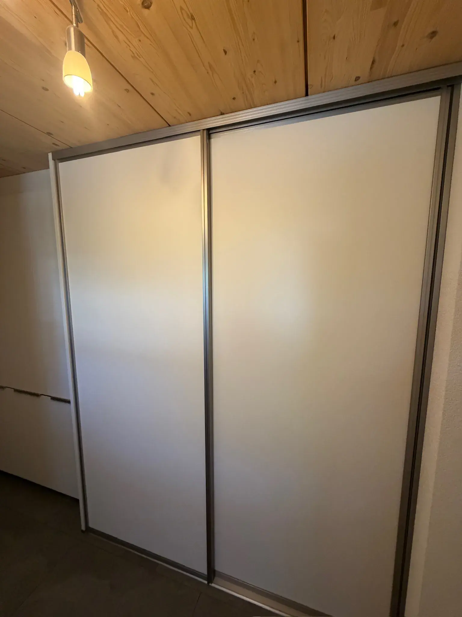 Schiebetürenschrank mit weißen Fronten unter Holzdecke