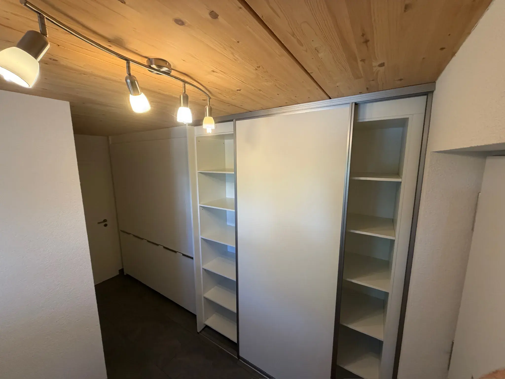 Kleiner Raum mit Holzdecke, weißen Regalen und moderner Deckenbeleuchtung.