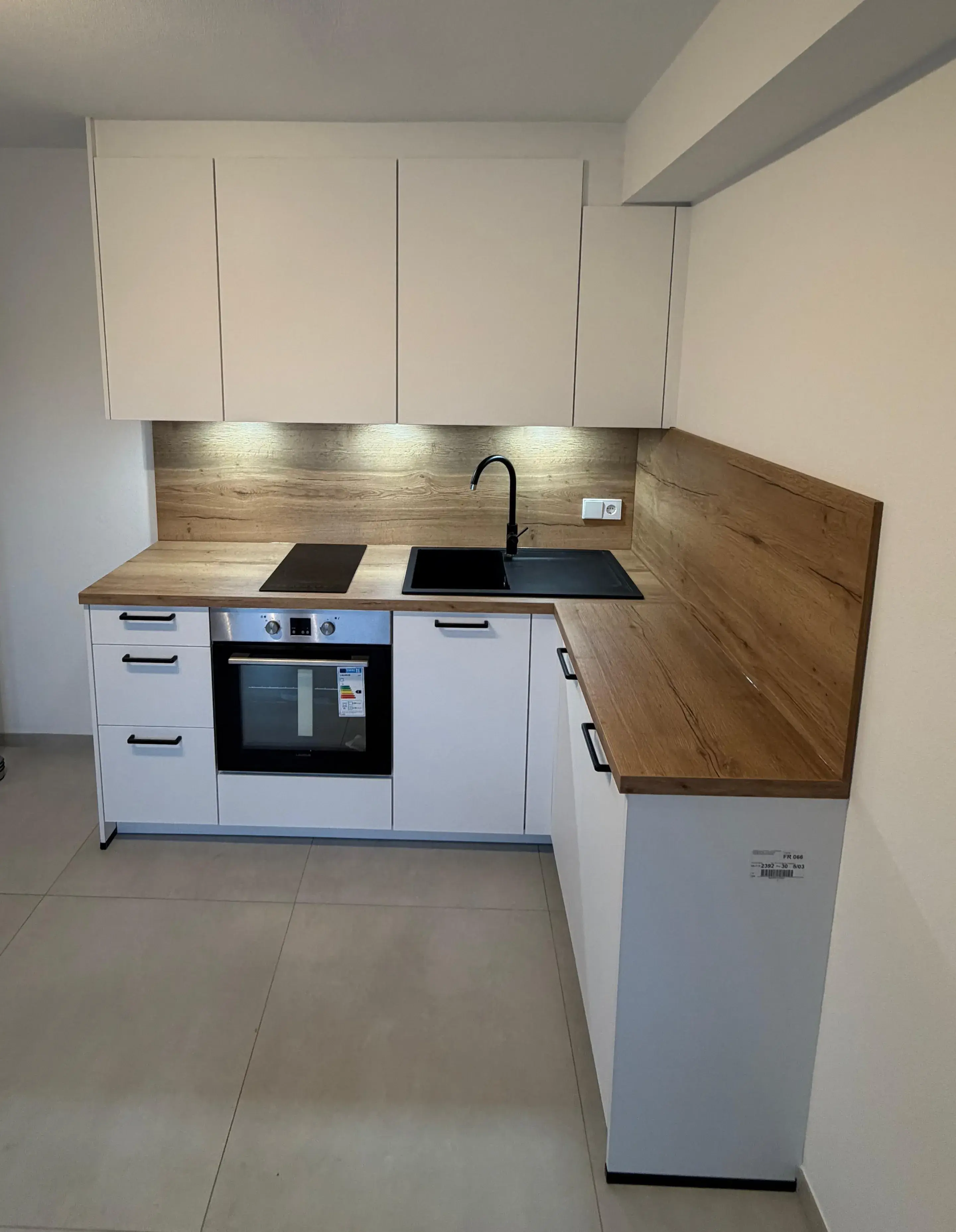 Moderne Einbauküche mit weißen Schränken und Holzarbeitsplatte.