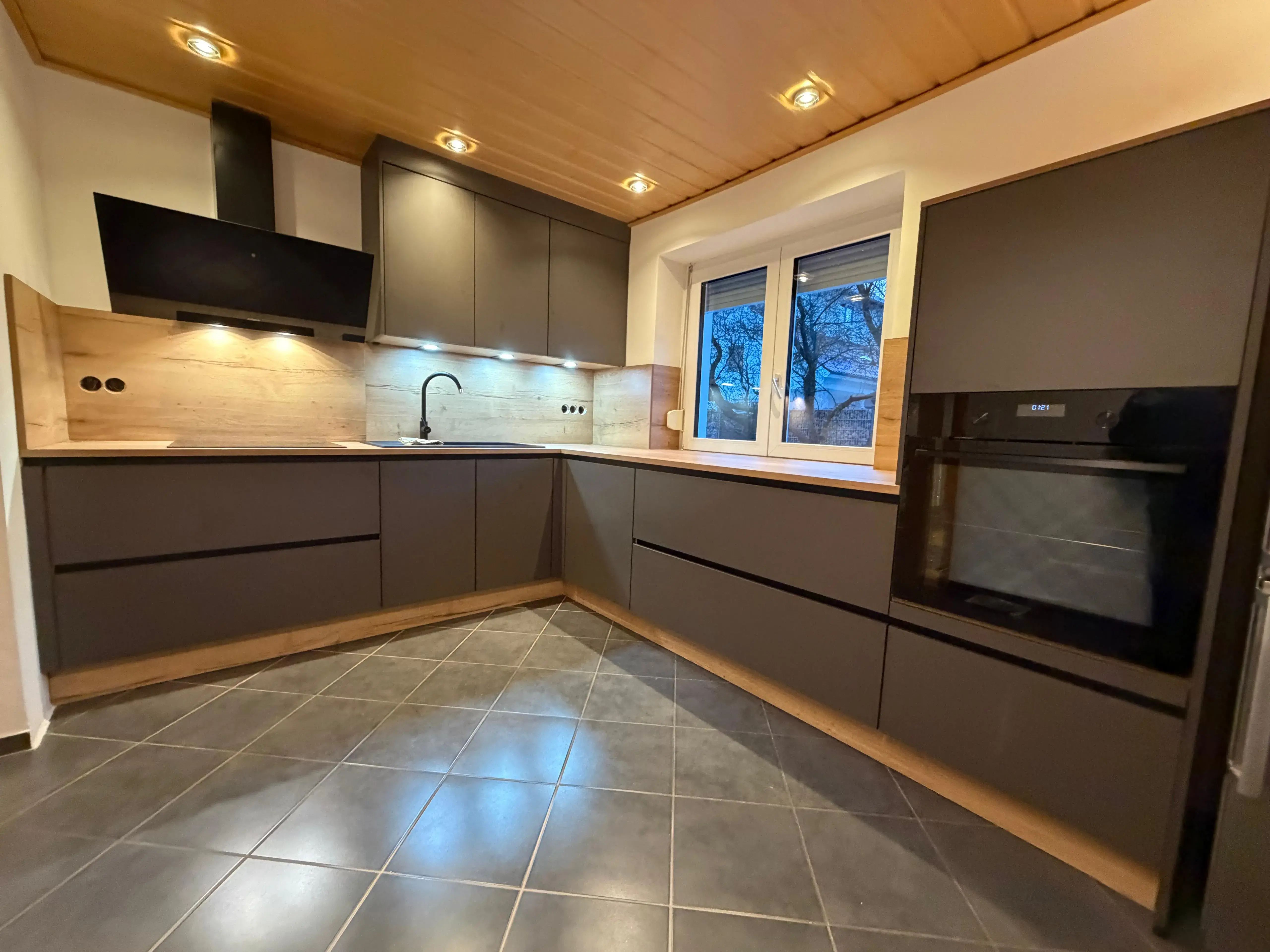 Moderne Küche mit dunklen Schränken, Holzdecke und eingebautem Ofen.