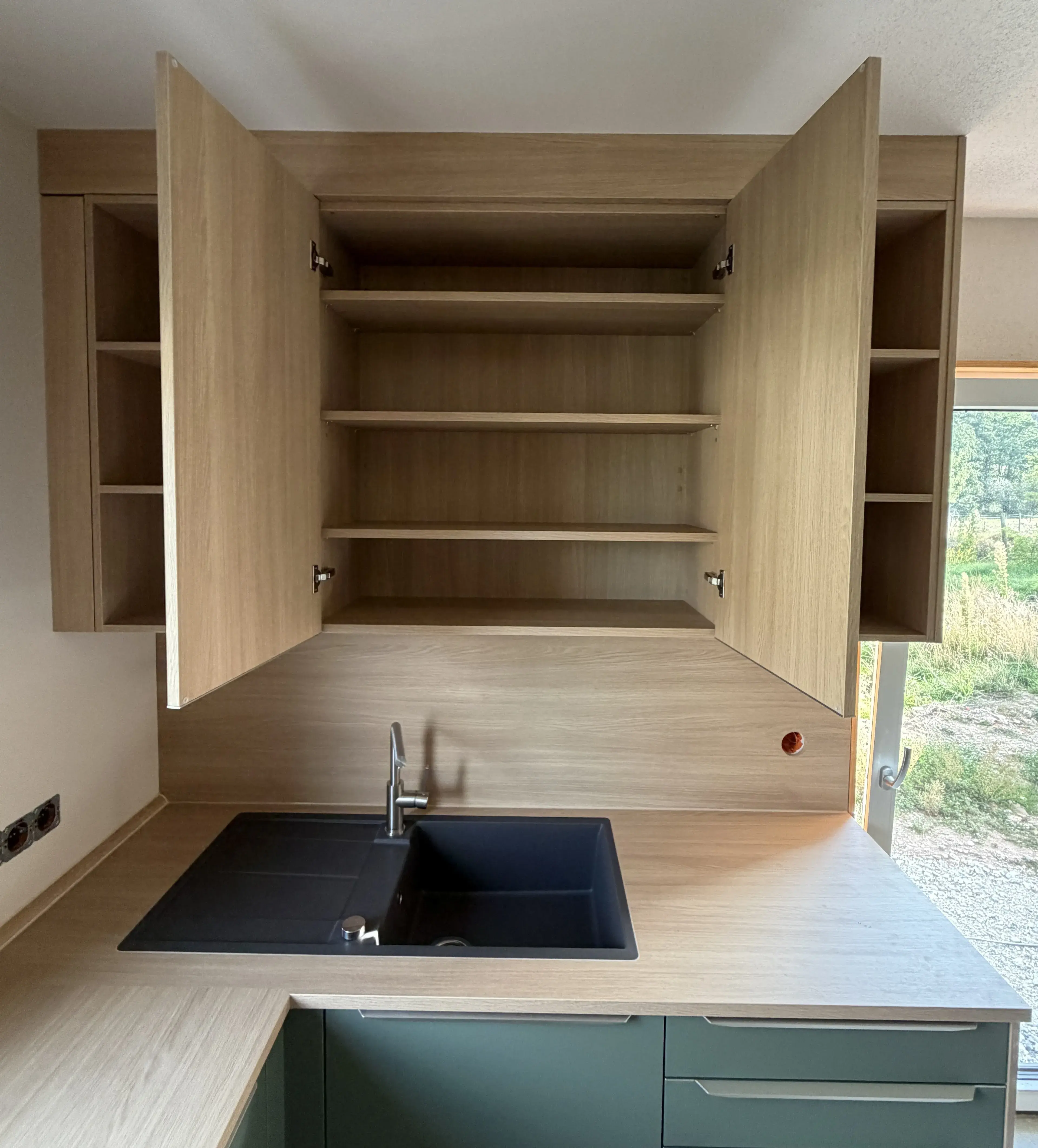 offener Hängeschrank in Holz schwarze spüle teilweise ist ene Terassentüre zu sehen