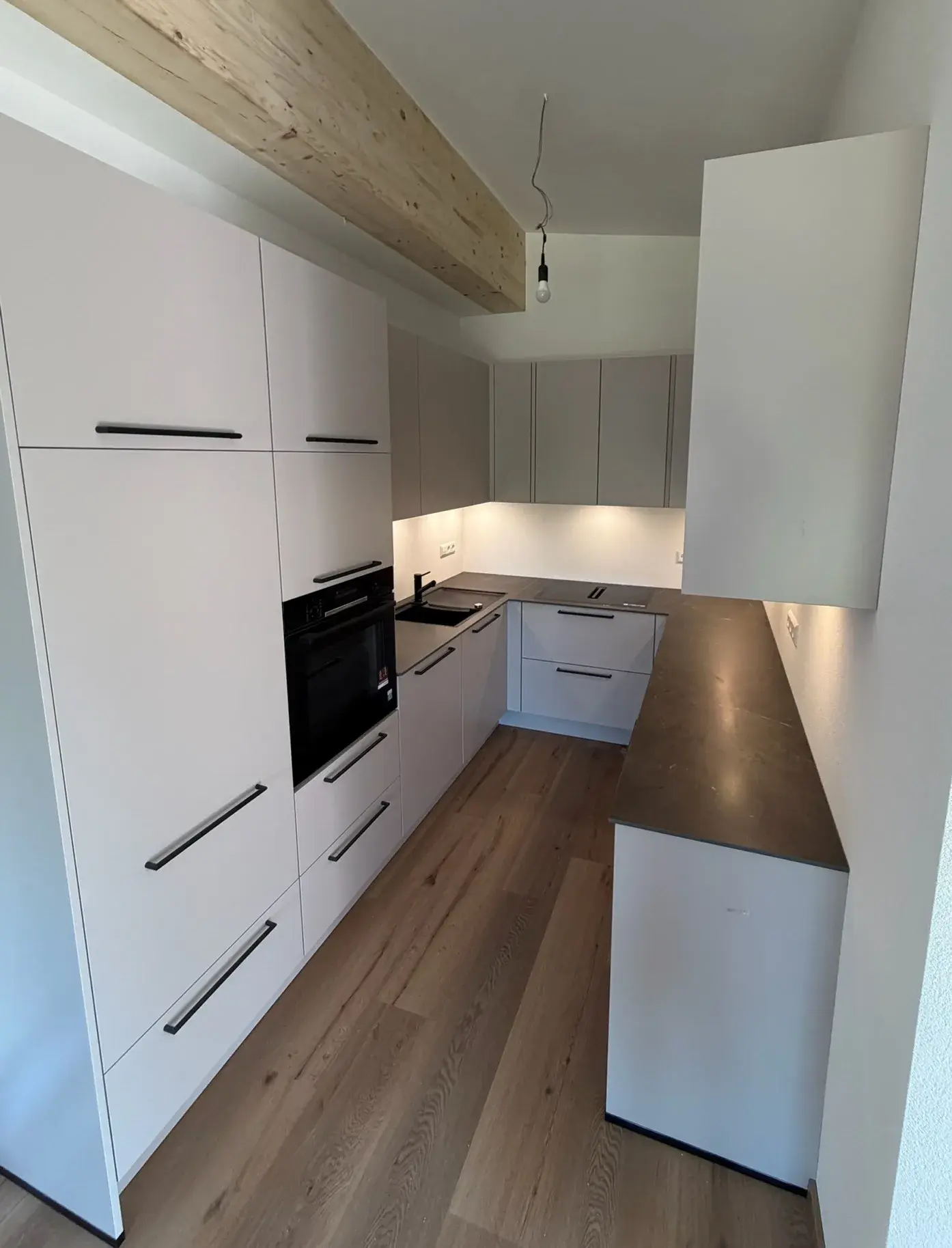 Holzboden, weisse Wände Küchenzeile in Uform, Schwarzer Backofen, Holzbalken an Decke